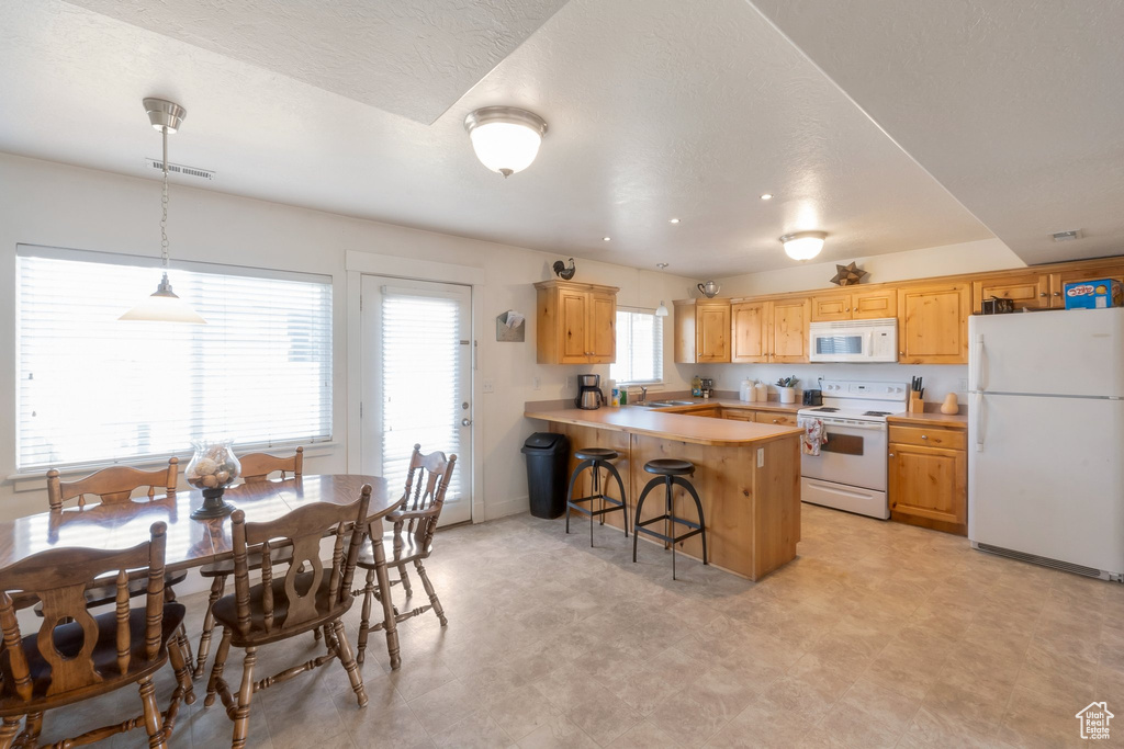 Kitchen featuring white appliances, light flooring, a peninsula, a kitchen bar, and light countertops