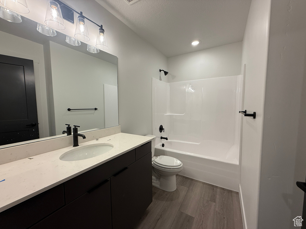 Bathroom with wood finished floors, toilet, vanity, shower / bathtub combination, and recessed lighting