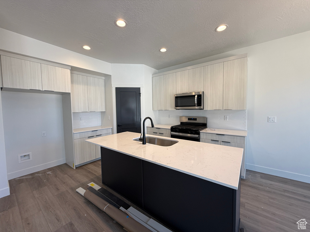 Kitchen featuring stainless steel appliances, a sink, modern cabinets, an island with sink, and dark wood-style floors