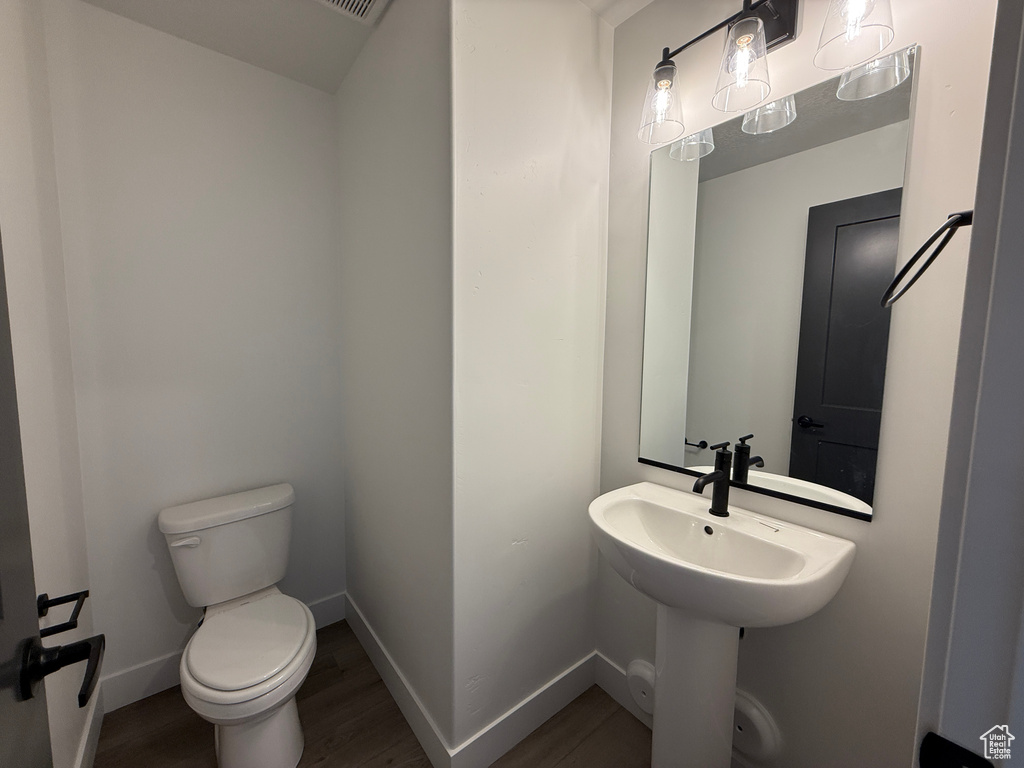Bathroom with toilet, wood finished floors, baseboards, and a sink