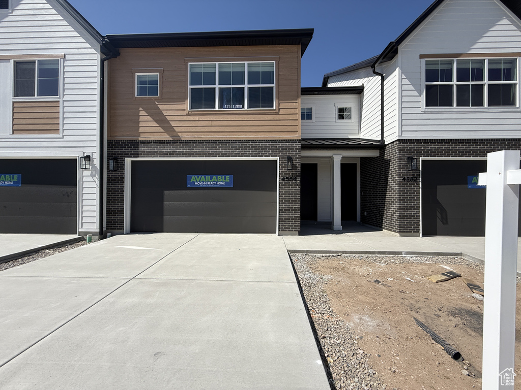 View of front of house featuring driveway, brick siding, a garage, a standing seam roof, and metal roof