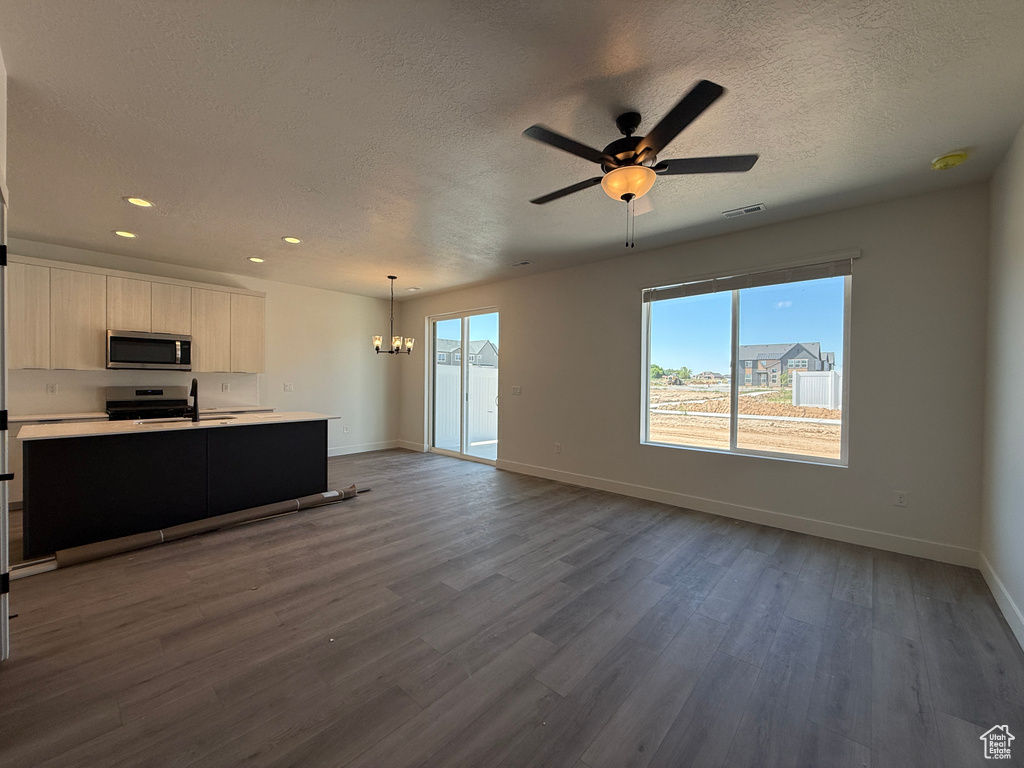 Unfurnished living room featuring baseboards, a textured ceiling, a chandelier, dark wood finished floors, and recessed lighting