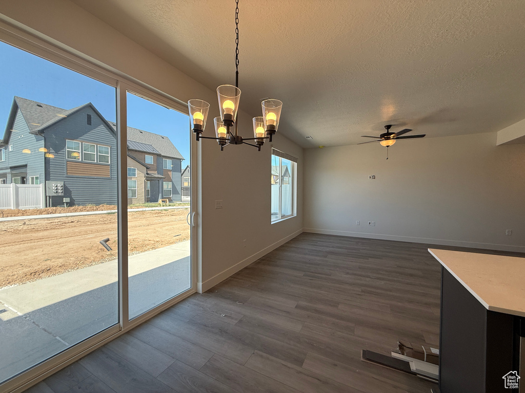 Unfurnished dining area featuring dark wood-style flooring, a chandelier, a textured ceiling, a ceiling fan, and baseboards