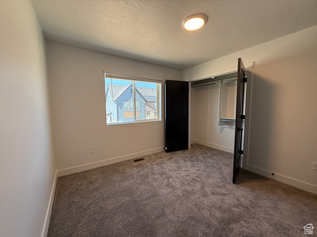 Unfurnished bedroom with a textured ceiling, carpet floors, baseboards, and a closet
