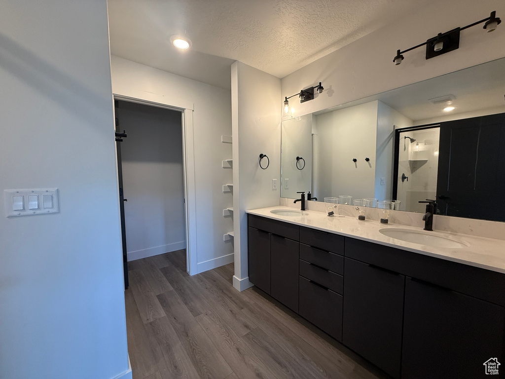Full bath with a stall shower, wood finished floors, double vanity, a textured ceiling, and baseboards