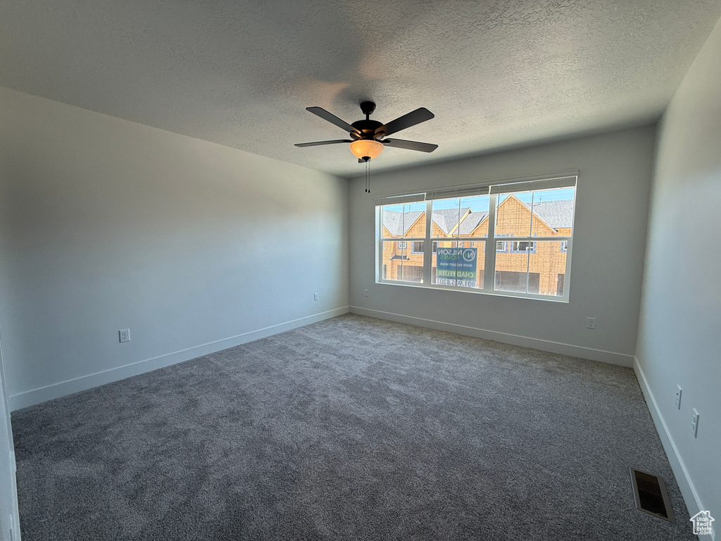 Carpeted empty room with a textured ceiling, a ceiling fan, and baseboards