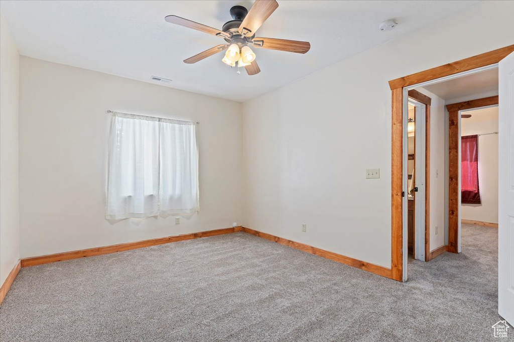 Carpeted spare room featuring baseboards, ceiling fan, and a smoke detector
