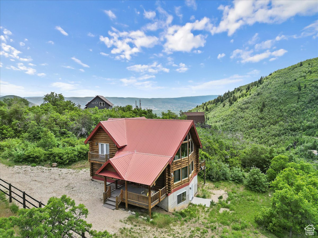 Back of property featuring log siding, a deck with water view, a wooded view, and metal roof