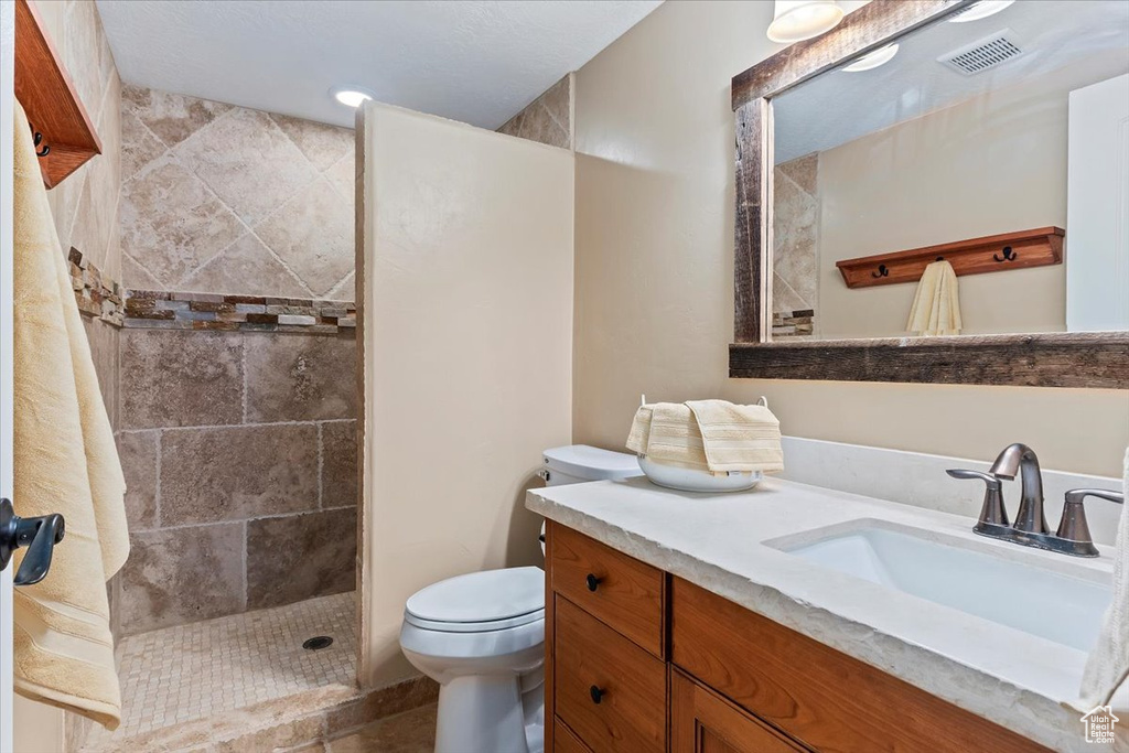 Bathroom featuring toilet, a tile shower, and vanity