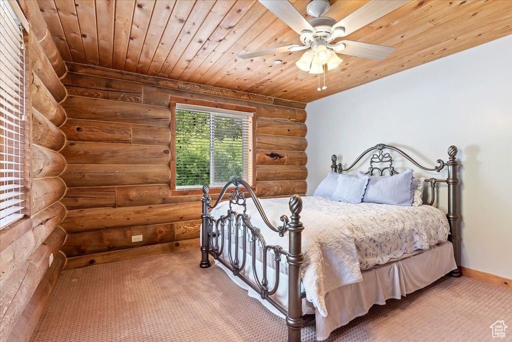 Carpeted bedroom with wood ceiling, rustic walls, baseboards, and ceiling fan