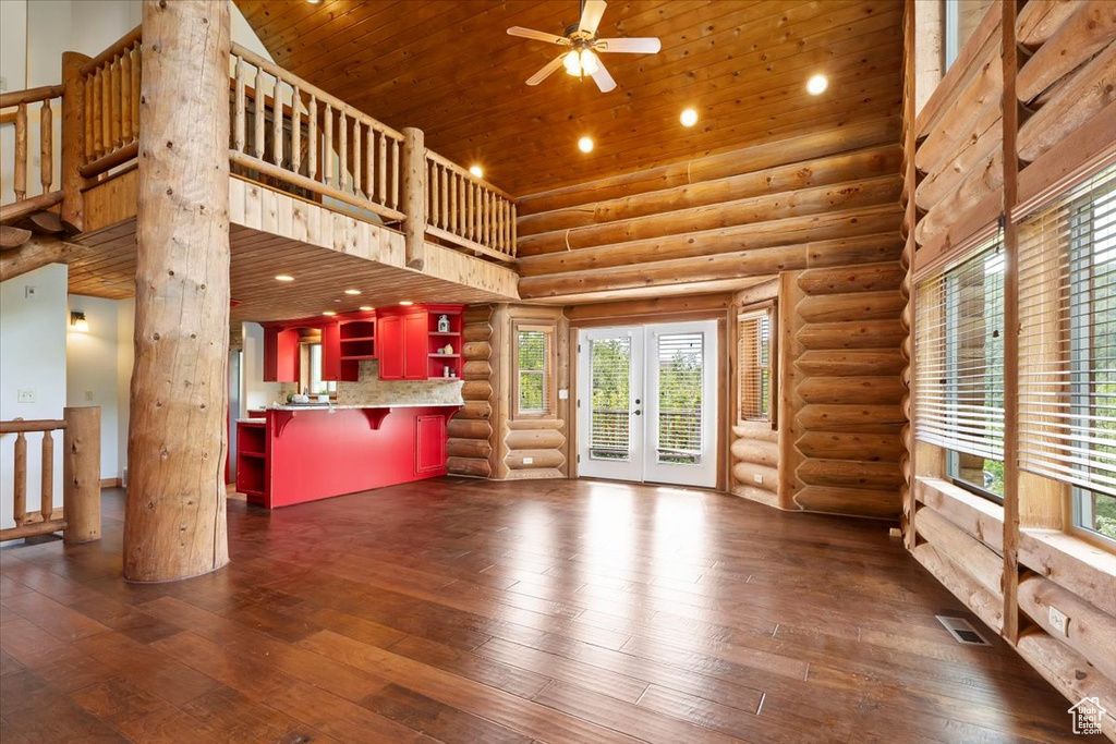 Unfurnished living room with dark wood-style floors, a towering ceiling, wood ceiling, log walls, and a ceiling fan