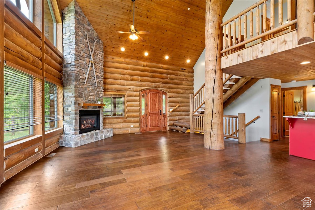 Unfurnished living room with high vaulted ceiling, log walls, wood-type flooring, a stone fireplace, and ceiling fan