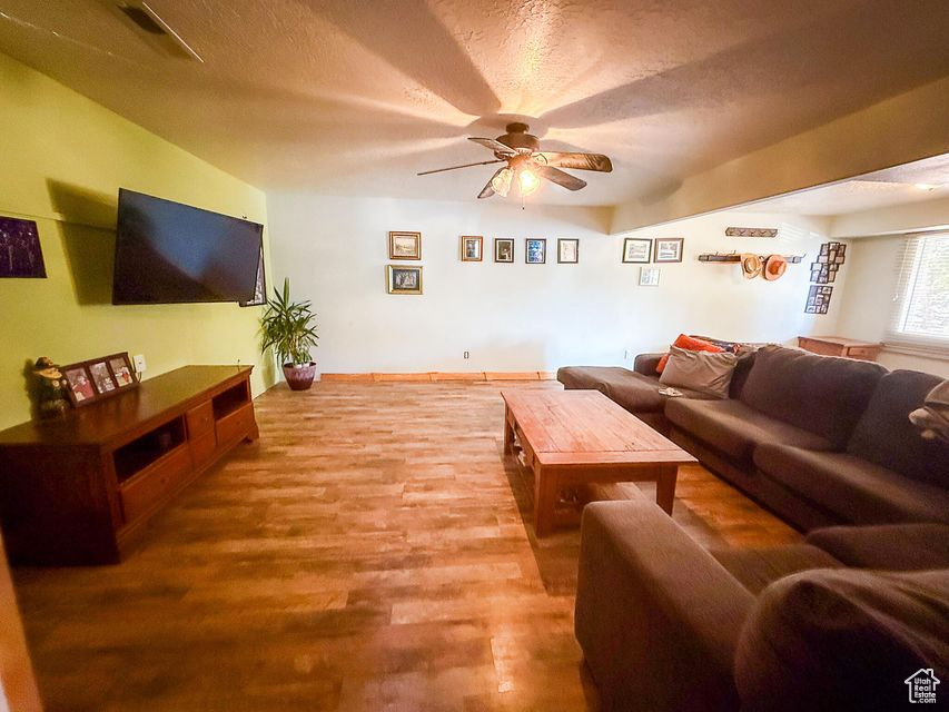 Living area with a ceiling fan, wood finished floors, and a textured ceiling