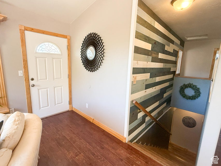 Entrance foyer with dark wood-style flooring, baseboards, and wood walls