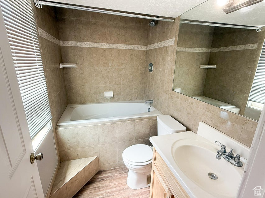 Full bathroom with toilet, tiled shower / bath combo, wood finished floors, vanity, and plenty of natural light