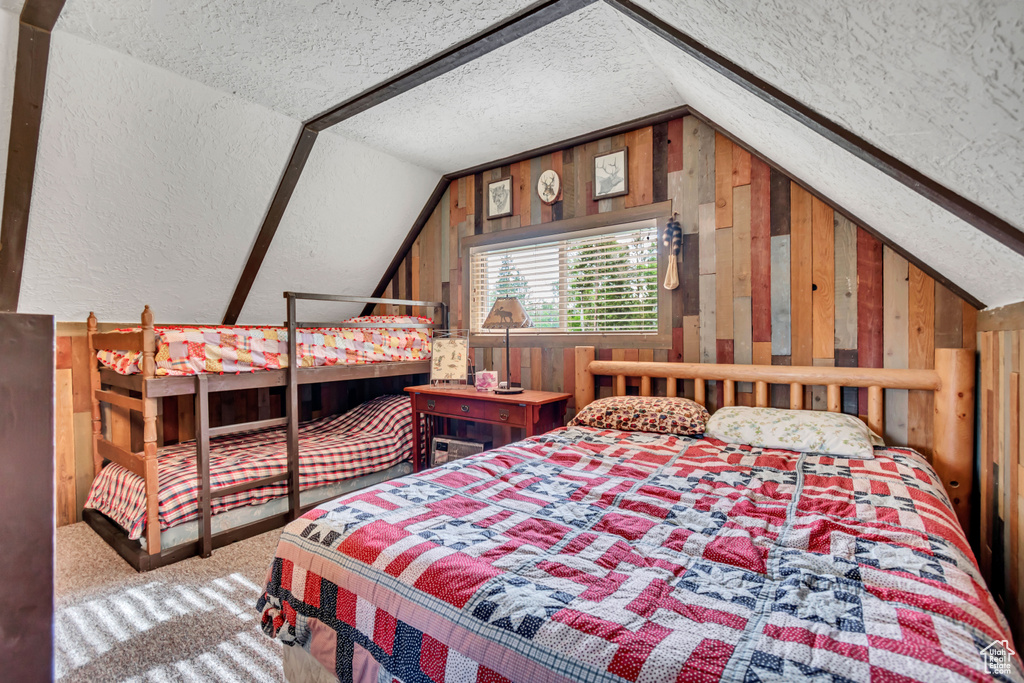 Bedroom with vaulted ceiling, a textured ceiling, wood walls, and carpet floors