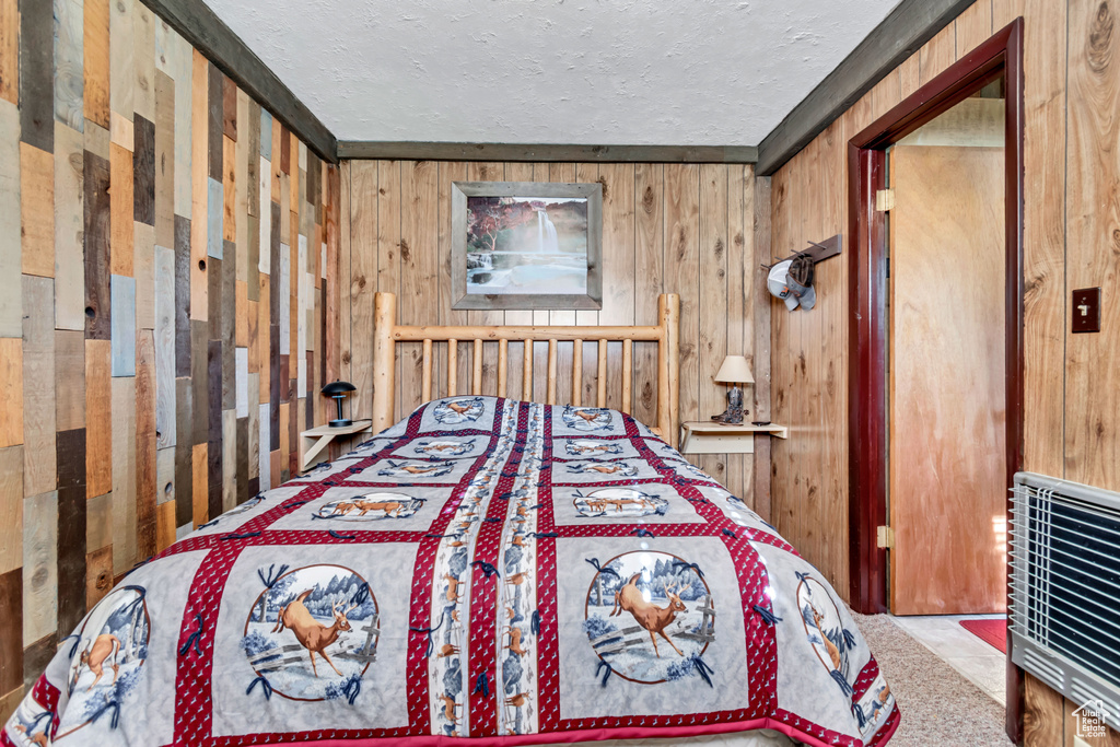 Bedroom with heating unit, wooden walls, and a textured ceiling