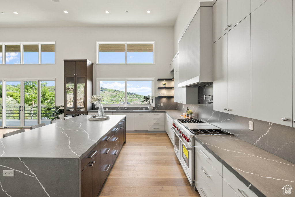 Kitchen with range with two ovens, wall chimney range hood, plenty of natural light, recessed lighting, and light wood-type flooring