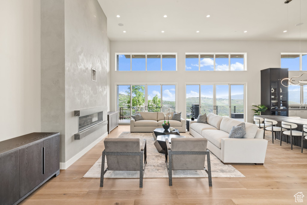 Living room with recessed lighting, healthy amount of natural light, light wood finished floors, a large fireplace, and a high ceiling