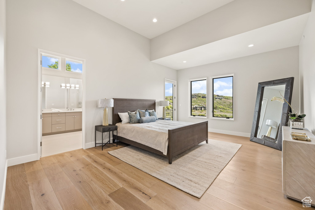Bedroom with multiple windows, light wood-style floors, baseboards, recessed lighting, and ensuite bath