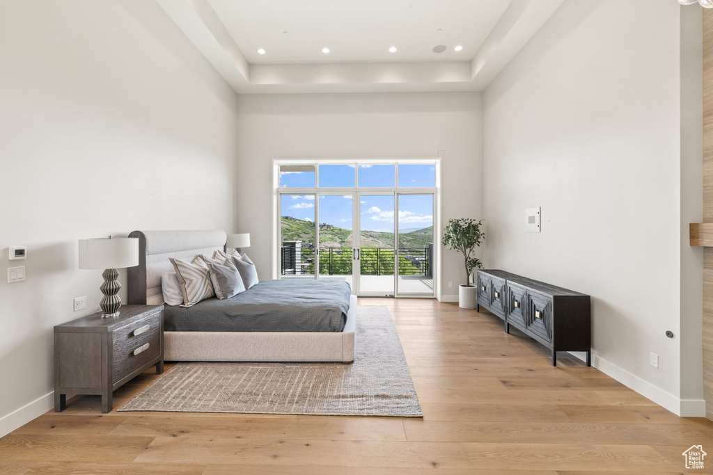 Bedroom with access to exterior, a high ceiling, light wood-style flooring, baseboards, and a raised ceiling