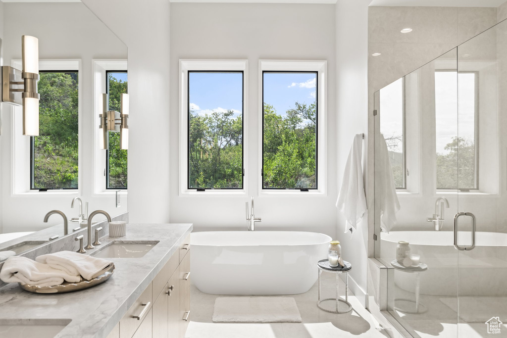 Full bathroom featuring double vanity, plenty of natural light, a freestanding bath, and a shower stall