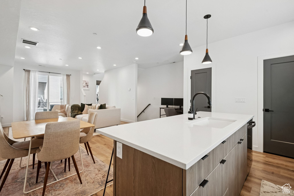 Kitchen featuring a sink, modern cabinets, a center island with sink, light wood finished floors, and recessed lighting