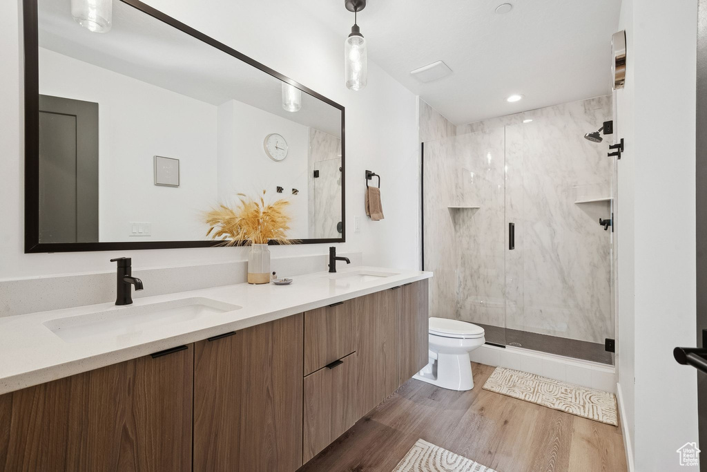 Bathroom with toilet, a marble finish shower, wood finished floors, and double vanity
