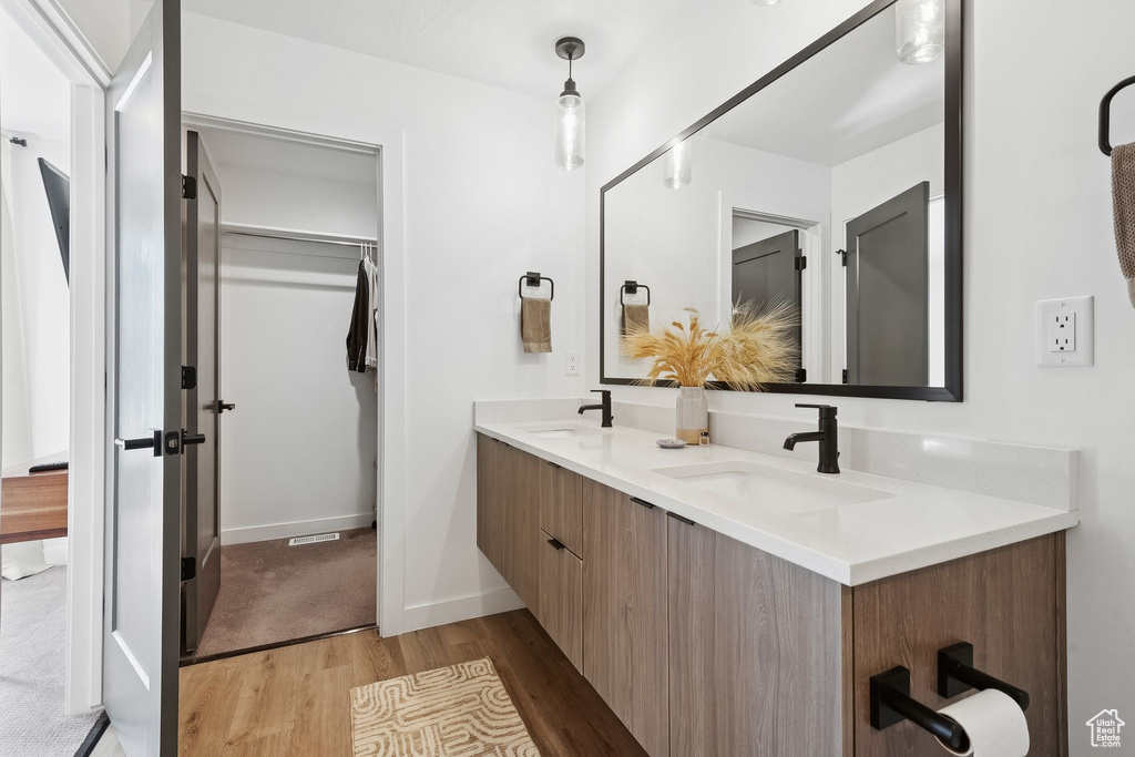 Full bathroom with wood finished floors, double vanity, a walk in closet, and baseboards
