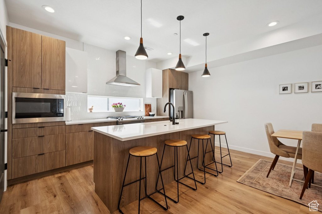 Kitchen with appliances with stainless steel finishes, modern cabinets, wall chimney range hood, a kitchen bar, and recessed lighting