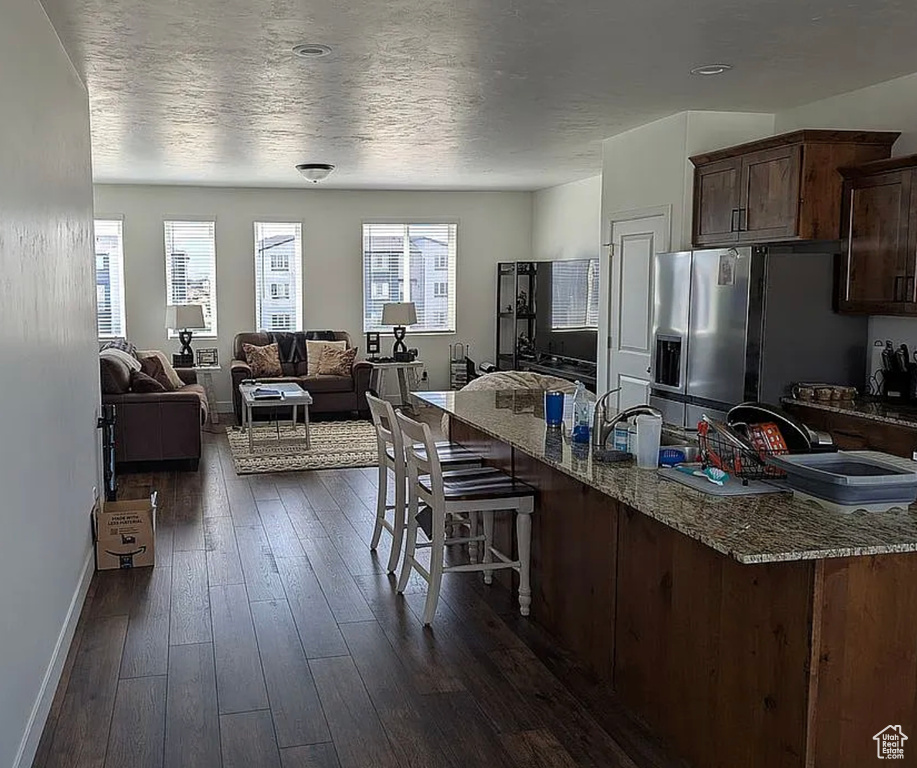 Kitchen with stainless steel refrigerator with ice dispenser, a breakfast bar area, baseboards, dark wood-style flooring, and stone countertops