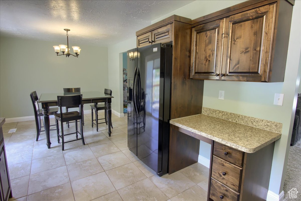 Kitchen with refrigerator with ice dispenser, a chandelier, light countertops, a textured ceiling, and pendant lighting