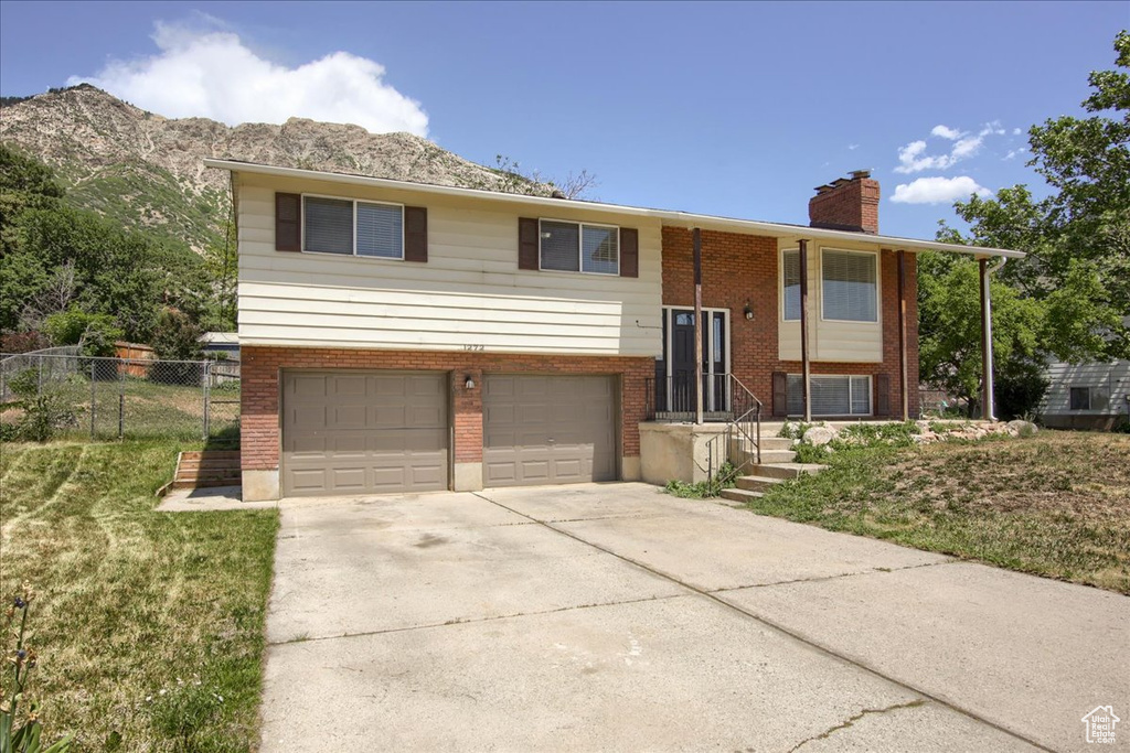 Bi-level home featuring a garage, a chimney, driveway, brick siding, and a mountain view