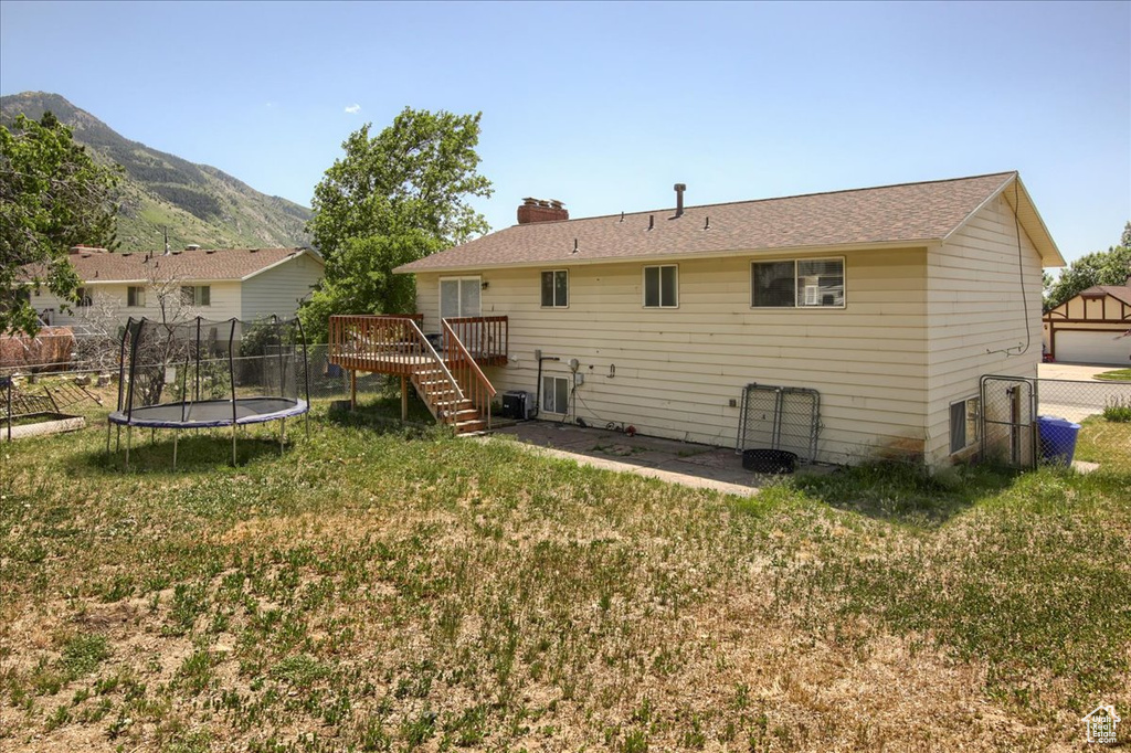 Rear view of house with a trampoline, a deck with mountain view, stairway, and a chimney