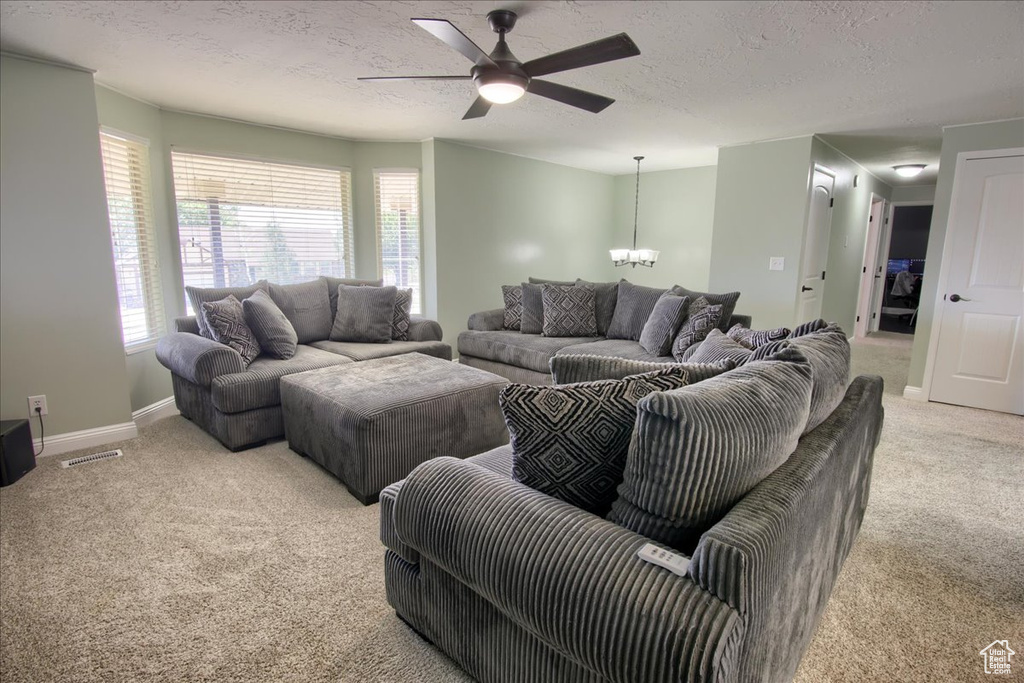 Living room with light colored carpet, a chandelier, a ceiling fan, a textured ceiling, and baseboards