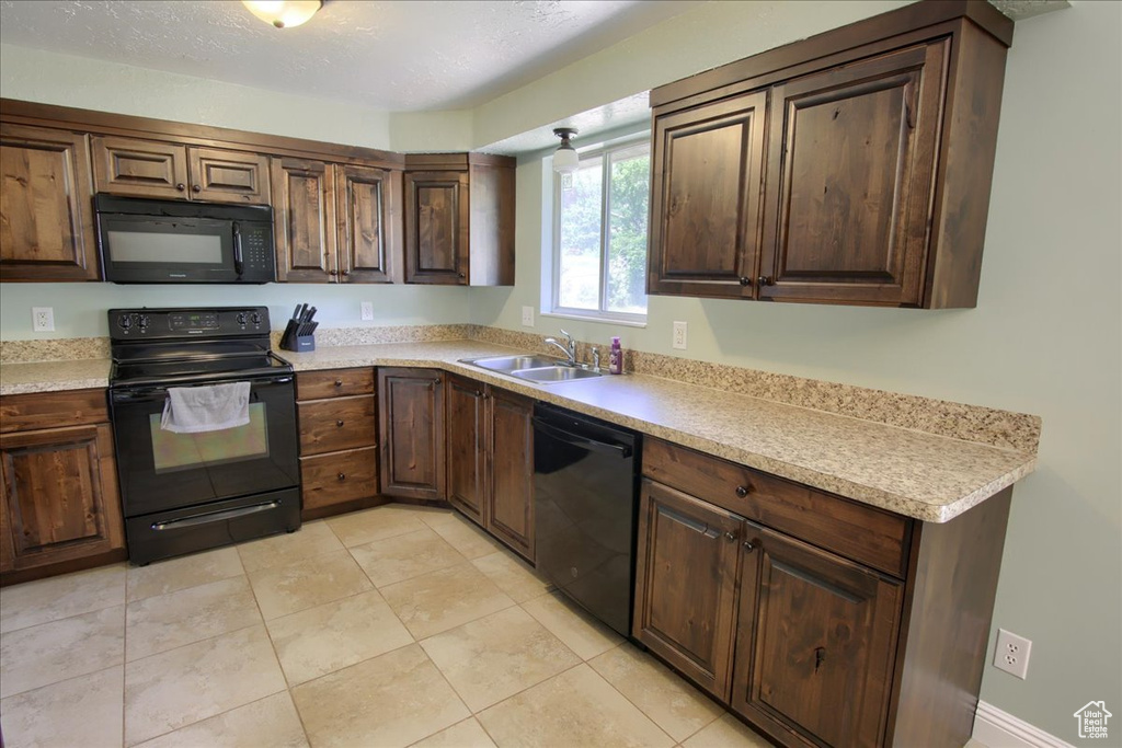 Kitchen with black appliances, a sink, light countertops, and light tile patterned flooring