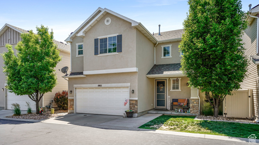 View of front of property featuring stone siding, stucco siding, a garage, concrete driveway, and roof with shingles