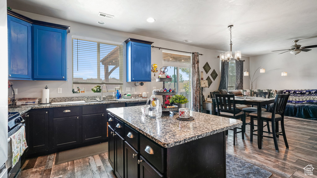 Kitchen with wood finished floors, a ceiling fan, stainless steel range with gas stovetop, a sink, and a center island