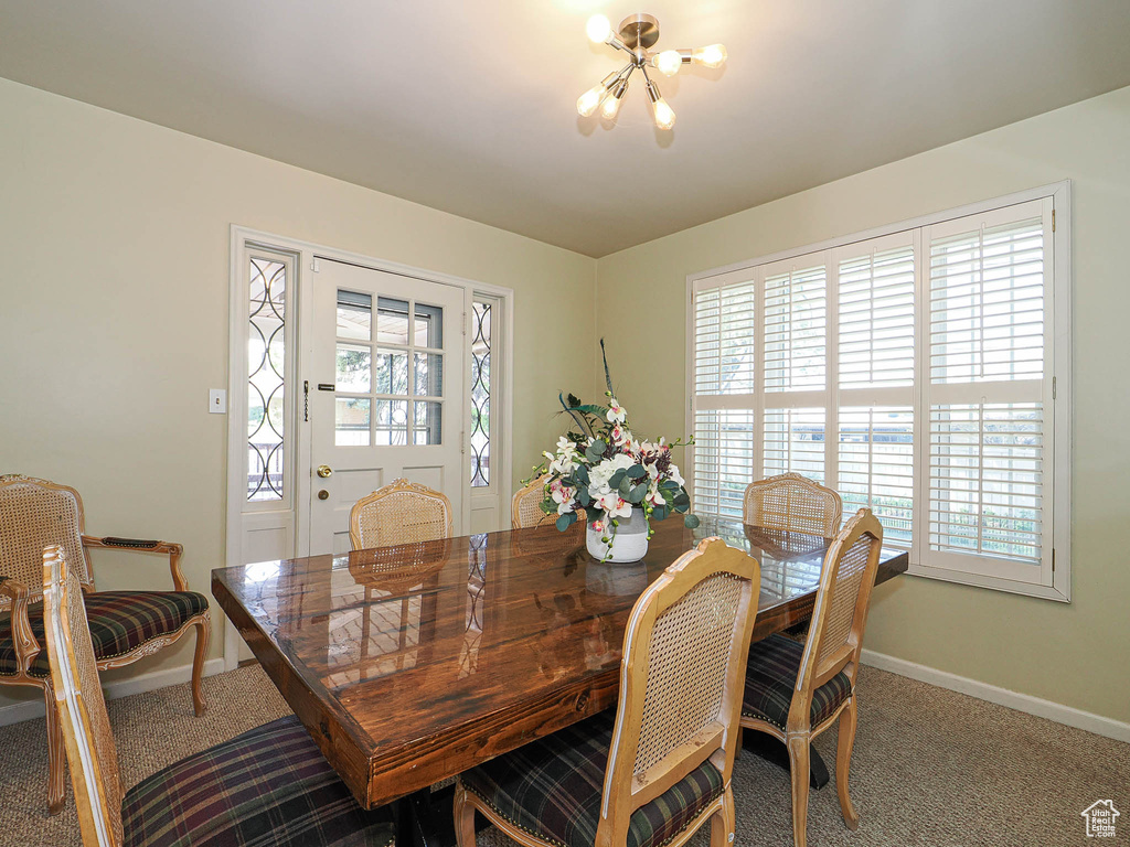 Carpeted dining area with a chandelier, baseboards, and healthy amount of natural light
