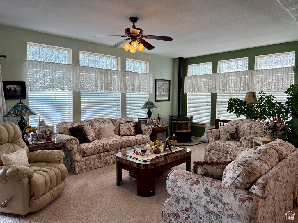 Carpeted living room featuring a wood stove, plenty of natural light, and a ceiling fan