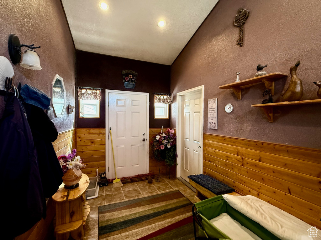 Entrance foyer featuring wainscoting, plenty of natural light, lofted ceiling, tile patterned flooring, and wood walls