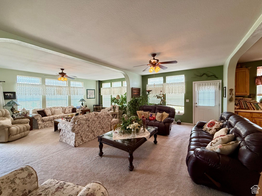 Living area with arched walkways, light carpet, ceiling fan, and a textured ceiling