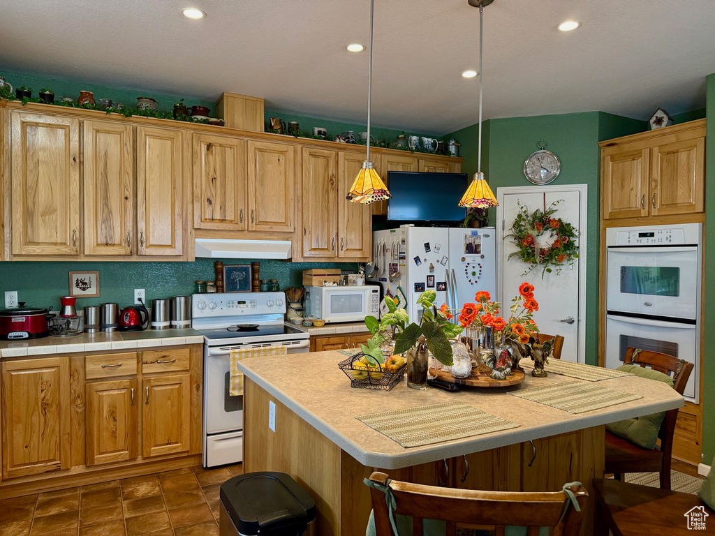Kitchen with white appliances, ventilation hood, recessed lighting, hanging light fixtures, and tile countertops