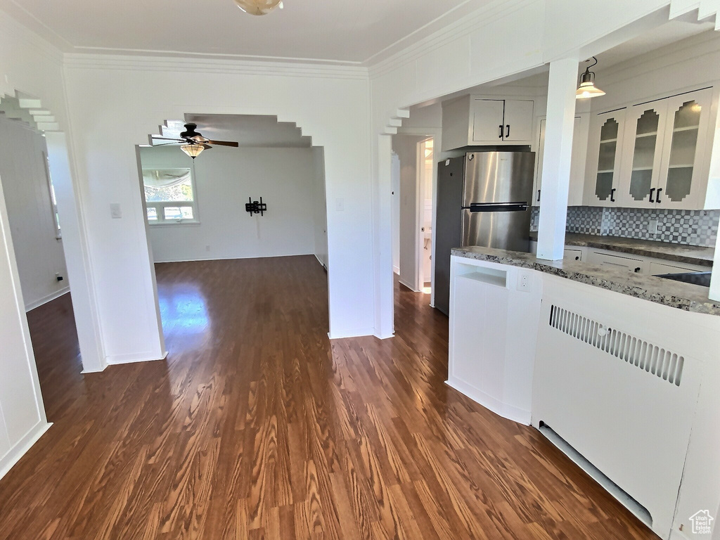Kitchen with crown molding, ceiling fan, arched walkways, dark stone counters, and glass insert cabinets