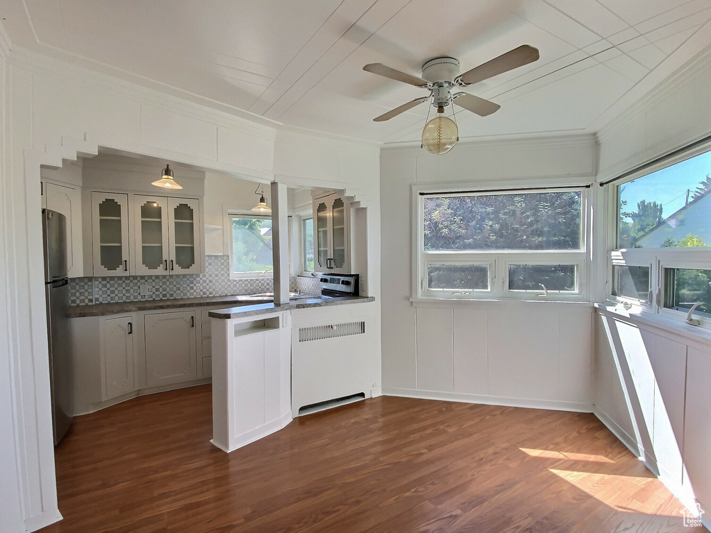 Kitchen with ornamental molding, glass insert cabinets, freestanding refrigerator, dark wood-style flooring, and a peninsula