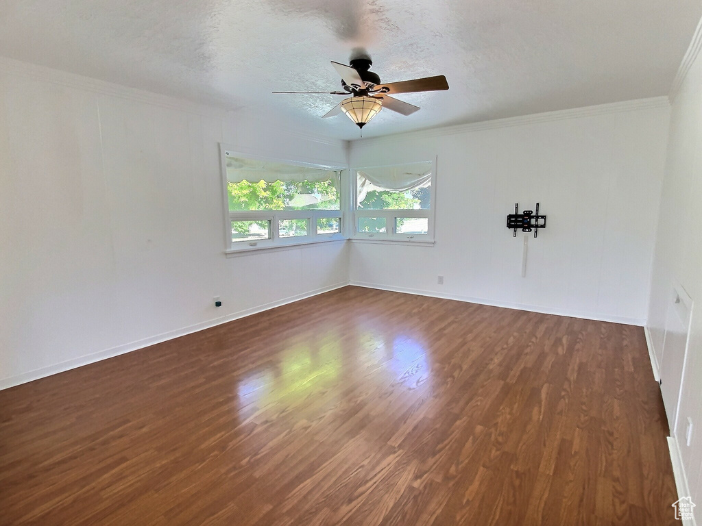 Spare room featuring ceiling fan, dark wood-style flooring, crown molding, baseboards, and a textured ceiling