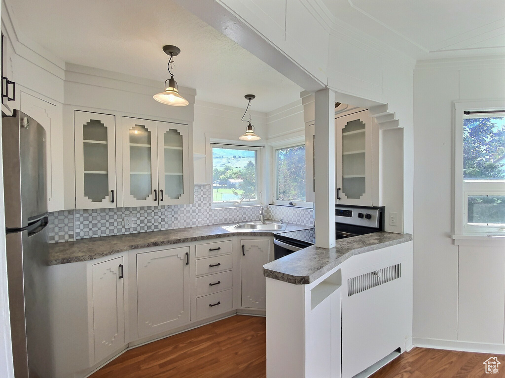 Kitchen featuring appliances with stainless steel finishes, a peninsula, backsplash, white cabinetry, and ornamental molding