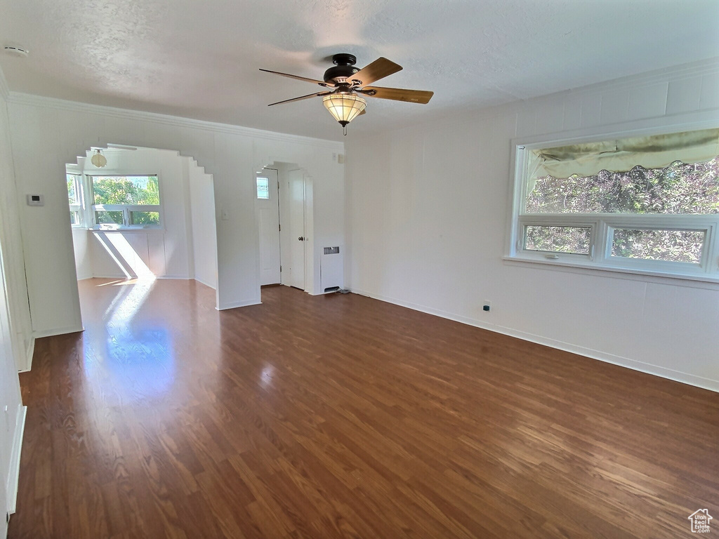 Unfurnished living room with dark wood-style floors, ceiling fan, baseboards, ornamental molding, and a textured ceiling