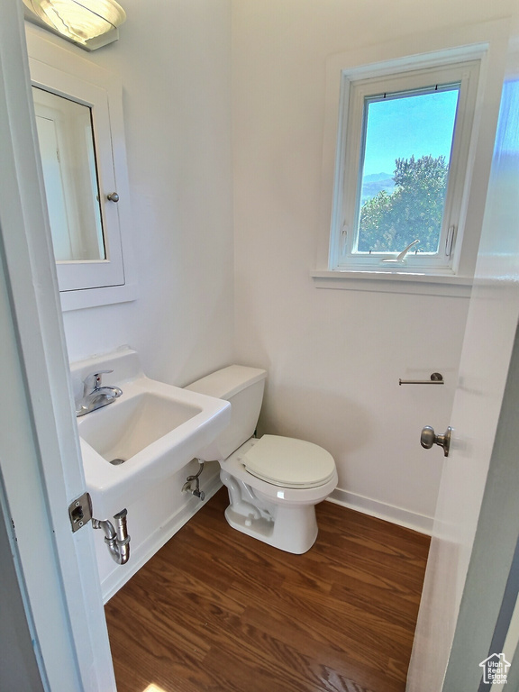 Half bath with a sink, toilet, wood finished floors, and baseboards