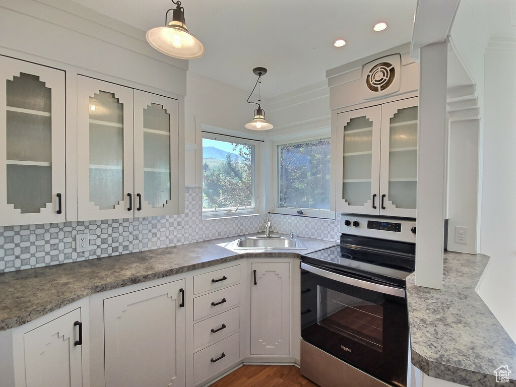 Kitchen with electric stove, a sink, decorative backsplash, white cabinetry, and crown molding